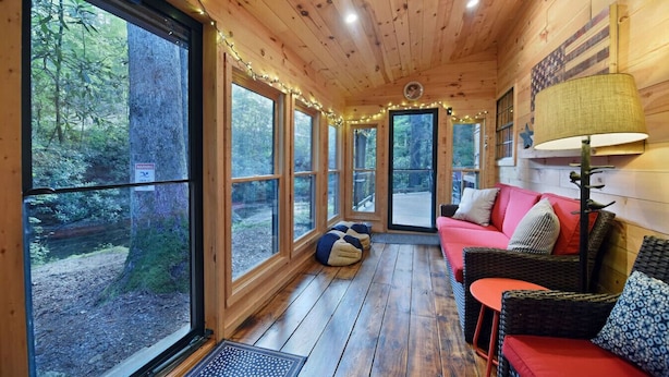 Ein Blockhaus-Interieur mit großen Fenstern, einer Holzbalkendecke, einem roten Sofa und einer Lampe.
