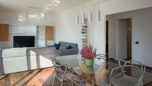 A modern living room with a sofa, a flat-screen TV, a dining area with a glass table and chairs, and a bookshelf. - VIlla Olivo - MyHomeinComo (Blevio)