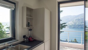 A modern kitchen with a built-in blender, a stainless steel sink, and a view of a lake and mountains through a large window. - VIlla Olivo - MyHomeinComo (Blevio)