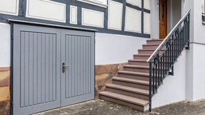 Un edificio con una puerta doble gris, una escalera con barandilla negra y una puerta de madera en la parte superior.
