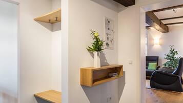 Un intérieur moderne avec un banc en bois, une étagère murale ornée d’un vase et un coin salon comprenant une chaise noire et une plante.