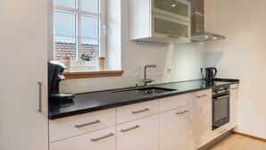 Una cocina moderna con encimera negra, electrodomésticos de acero inoxidable y ventana con vistas a un edificio.
