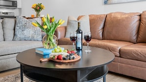 Una sala de estar moderna con un sofá de cuero, una mesa de centro redonda con una bandeja de frutas, una botella de vino y un florero.