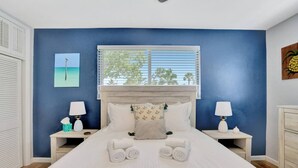 A bedroom with a large bed, two bedside tables with lamps, a window with blinds, and a painting on the wall. - Eagle`s Way: Heated Pool, Firepit & Sunroom Near BEACH! (North Palm Beach)