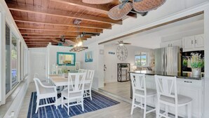 A spacious kitchen with white cabinetry, a stainless steel refrigerator, and a dining area with white chairs and a blue rug. - Eagle`s Way: Heated Pool, Firepit & Sunroom Near BEACH! (North Palm Beach)