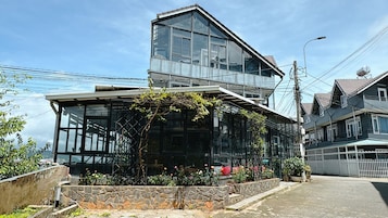 Una casa moderna de dos pisos con amplios ventanales, base de piedra y un pequeño jardín con flores.