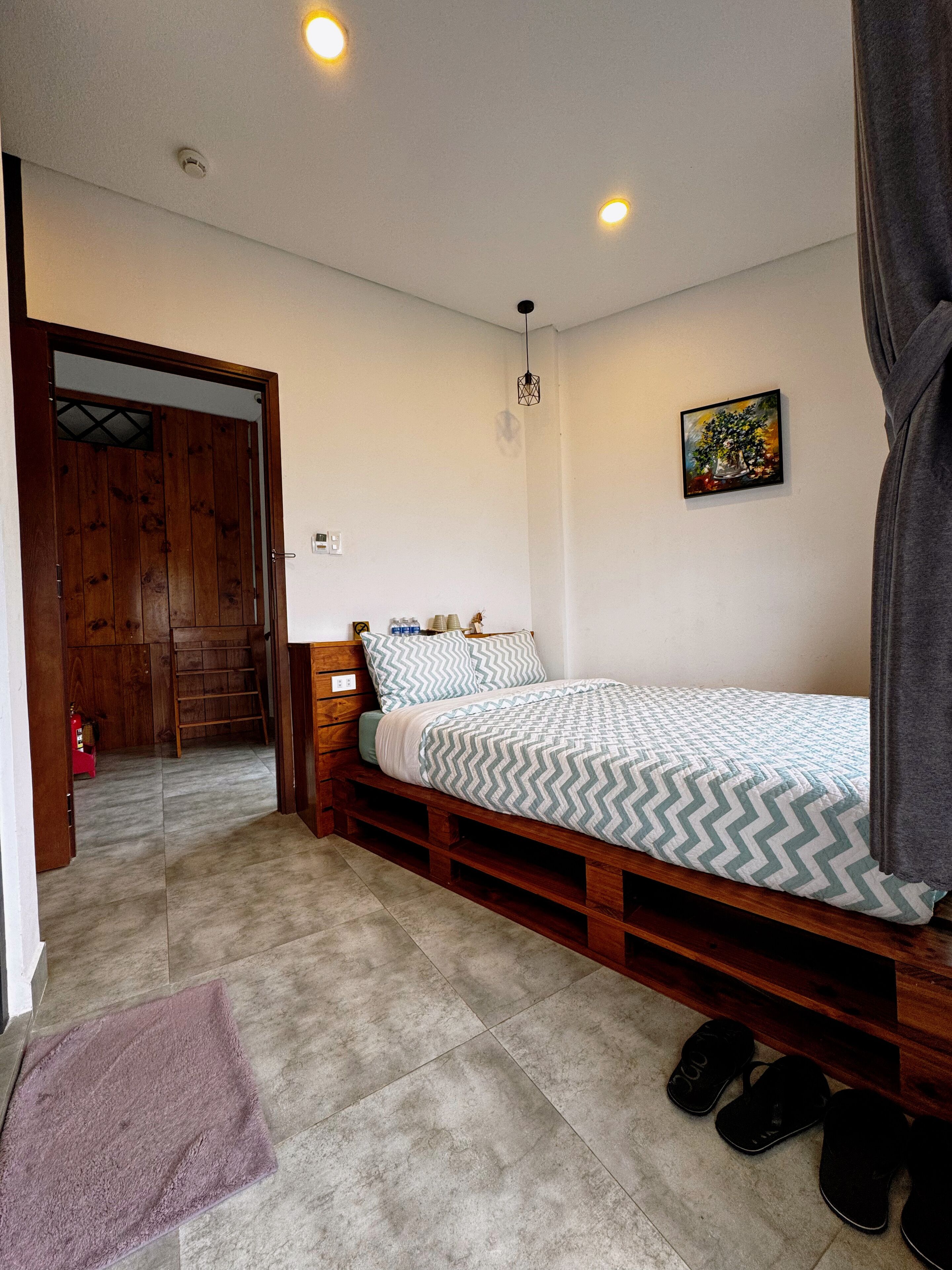A bedroom with a bed, a wooden bench, a small table with cups, and a painting on the wall.