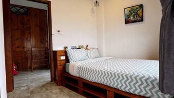 A bedroom with a bed, a wooden bench, a small table with cups, and a painting on the wall.