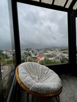 Una habitación con un ventanal que da a una zona residencial y una silla con un cojín mullido.