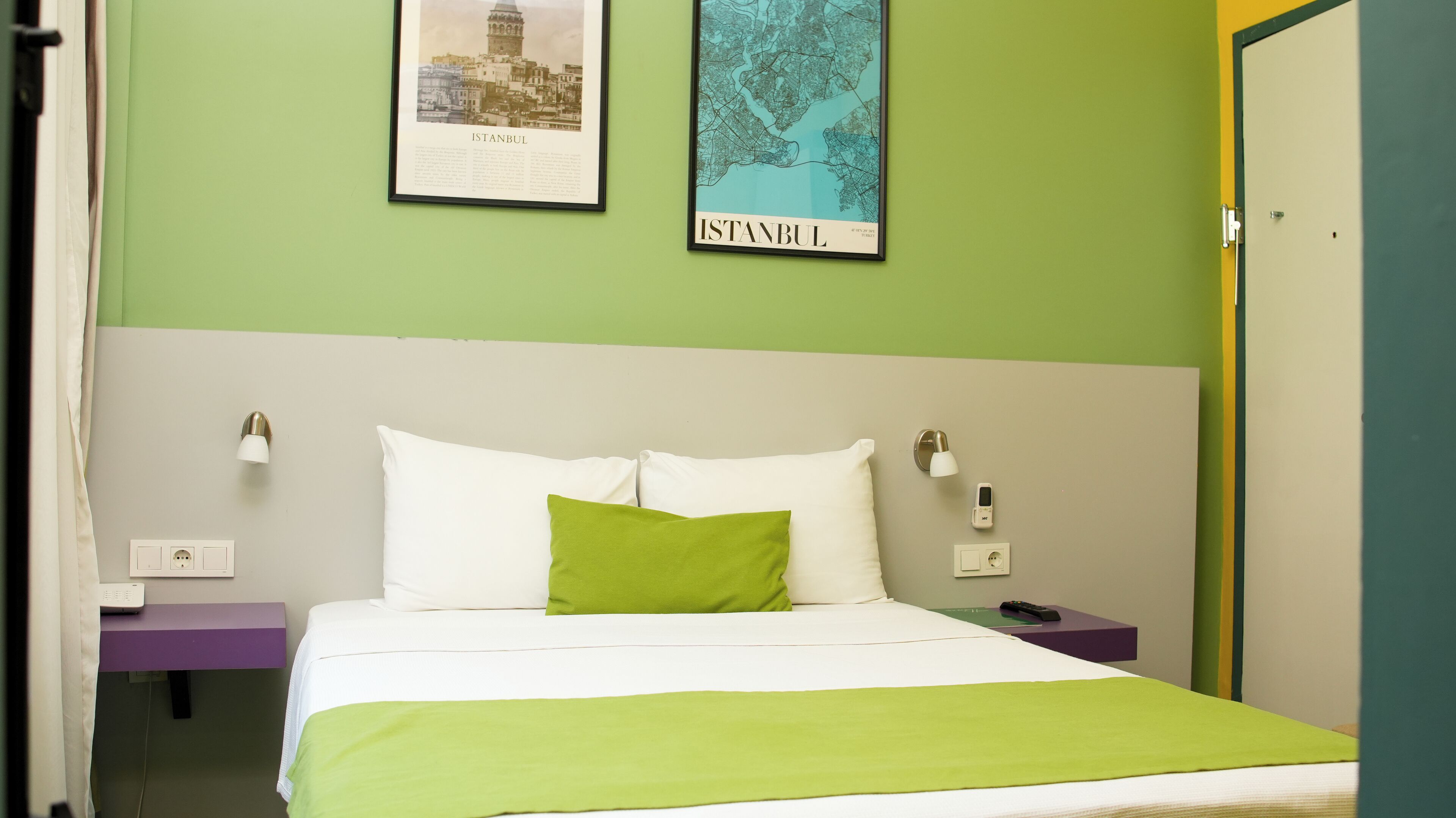 A hotel room with a bed, green walls, a framed map of Istanbul, and a door to the right.