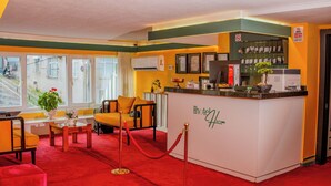 A hotel reception area with a red carpet, a reception desk, a seating area with a sofa and chairs, and a window with a view of the street. - Mini Harem Hotel (Istanbul)