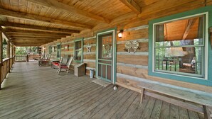 Eine Holzblockhütte mit einer Holzdielen-Terrasse, Sitzgelegenheiten im Freien und einem Willkommen-Schild.