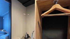 A hotel room with a bed, a small kitchenette with a kettle and a coffee maker, and a wooden hanger on a wall. - Hotel Kototoi Juku (Tokyo)