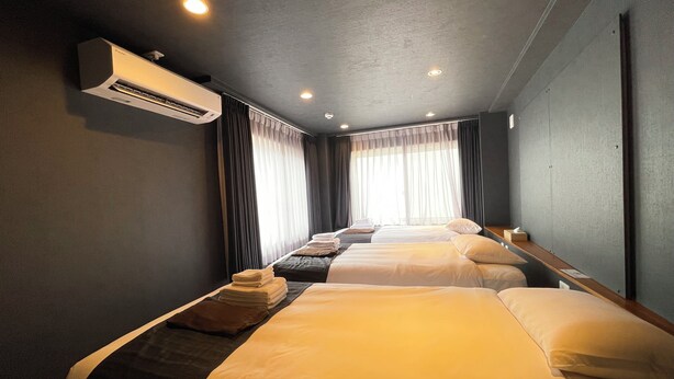 A hotel room with two beds, a flat-screen TV, an air conditioning unit, and a large window with curtains. - Hotel Kototoi Juku (Tokyo)