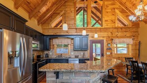 A spacious kitchen with a granite island, stainless steel appliances, and wooden beams. - One Day More (Banner Elk)