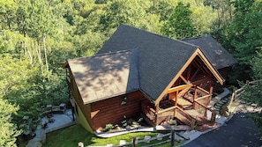 A log cabin with a steeply pitched roof, a wooden deck, and a stone pathway leading to the entrance. - One Day More (Banner Elk)