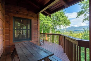 A wooden deck with a picnic table and a rocking chair, overlooking a forested mountain landscape. - One Day More (Banner Elk)