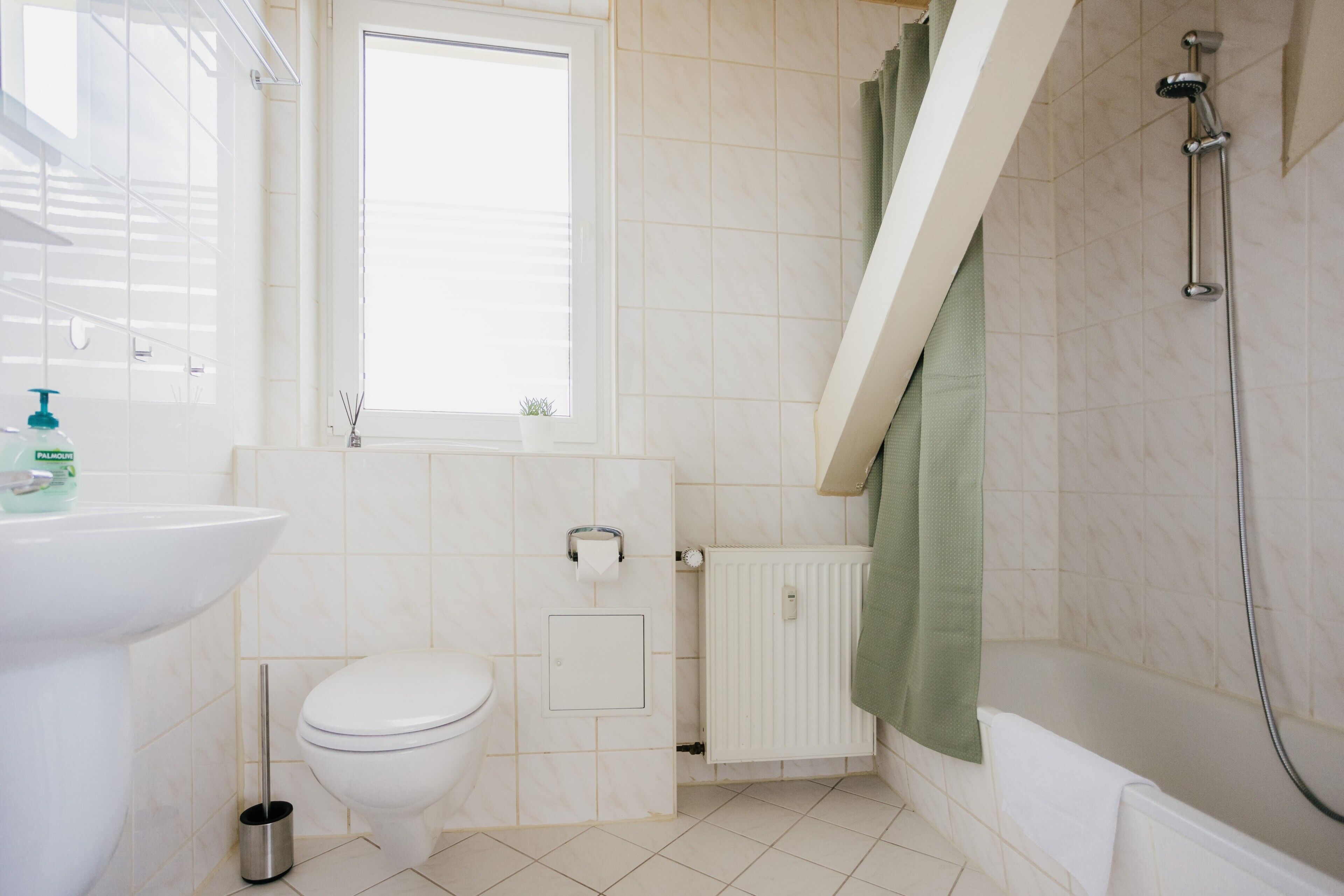 A bathroom with a toilet, sink, shower, and a window.