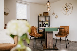 Comedor con mesa de madera, dos sillas de cuero marrón, mantel verde y lámpara colgante.