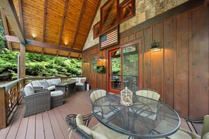 An outdoor patio with wicker furniture, a round metal table, and a wooden deck. - River Sound Cabin at Eagles Nest (Elk Park)