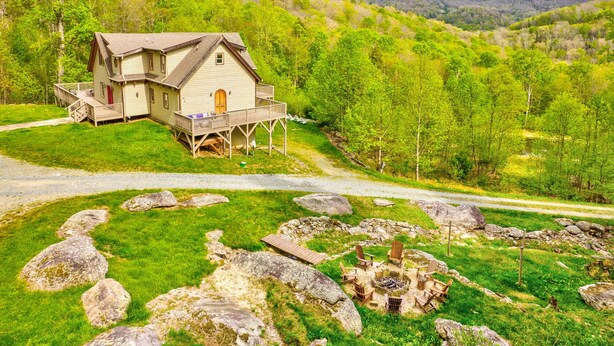 Une cabane dotée d’une terrasse, entourée d’une zone herbeuse parsemée de rochers et comprenant un foyer.