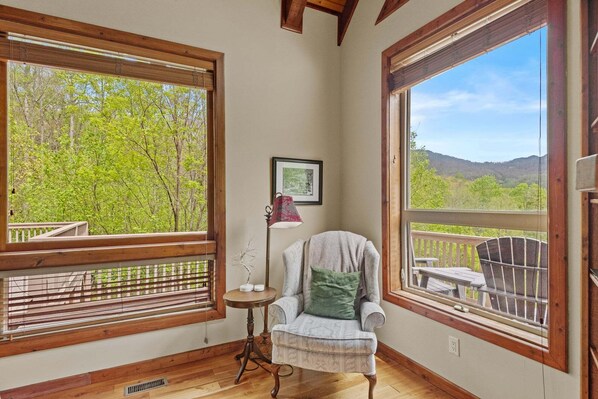 A room with large windows, a chair, a small table, and a lamp. - Stoneledge Manor (Banner Elk)