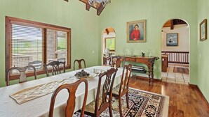 Une salle à manger avec une longue table, des chaises, un lustre et un tableau accroché au mur.