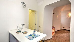 A hotel room with a white desk, a small chair, a mirror, and a door leading to another room.