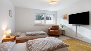 Ein Schlafzimmer mit zwei Betten, einem Sessel, einem Fernseher und einem Fenster.