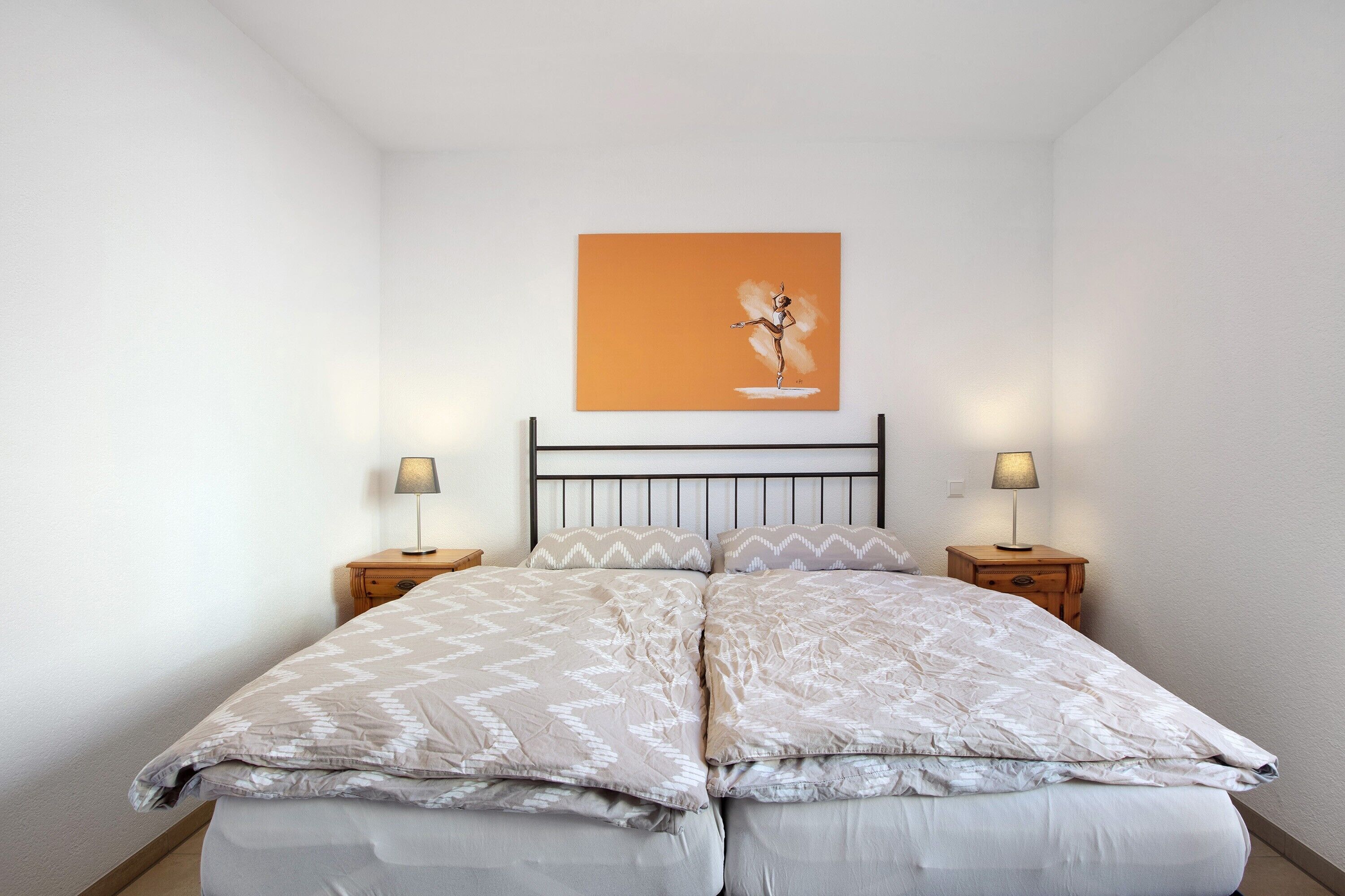 Un lit double avec une literie à motifs, deux tables de chevet avec des lampes et une œuvre d’art accrochée au mur.