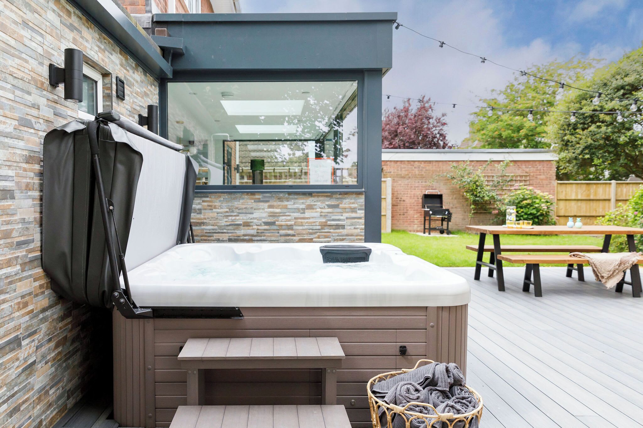 A hot tub on a wooden deck with a brick wall and a wooden fence in the background.