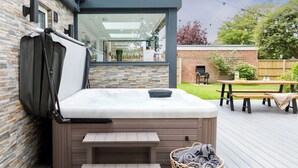 A hot tub on a wooden deck with a brick wall and a wooden fence in the background. - Coastal Retreat for 10 with Hot Tub (West Wittering)