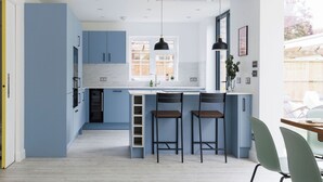 A modern kitchen with blue cabinets, a white countertop, and two bar stools. - Coastal Retreat for 10 with Hot Tub (West Wittering)