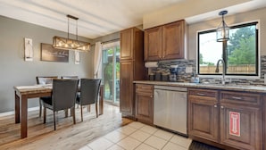 A modern kitchen with wooden cabinets, a dishwasher, and a dining area with a table and chairs. - Victory Mountain (Colorado Springs)