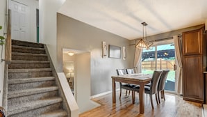 A dining area with a wooden table and chairs, a staircase, and a view of the outdoors. - Victory Mountain (Colorado Springs)