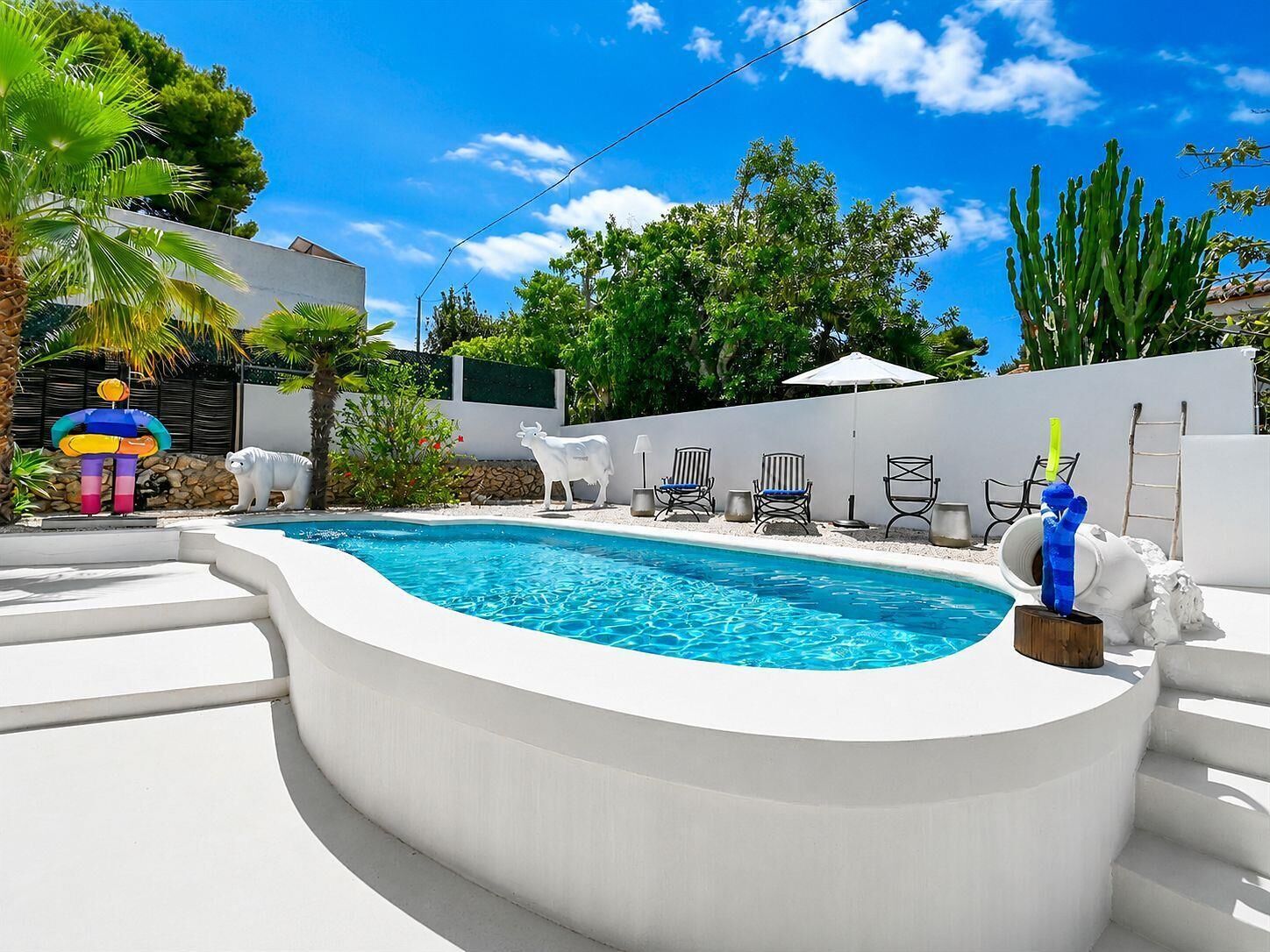 A swimming pool with a white deck, surrounded by lounge chairs and a decorative statue.