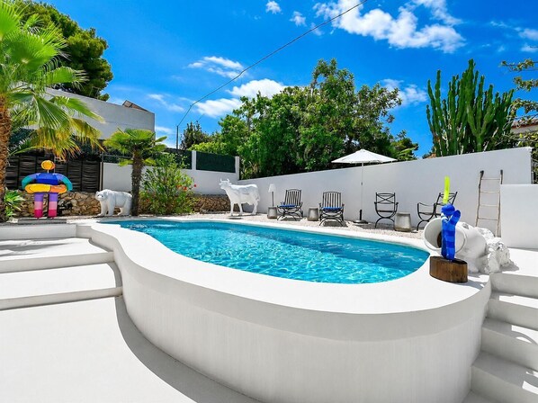 A swimming pool with a white deck, surrounded by lounge chairs and a decorative statue.