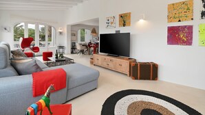 A modern living room with a grey sofa, red chairs, a television, and artwork on the walls.