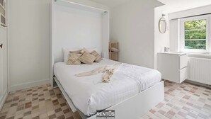 Quarto com cama, mesa de cabeceira, espelho e janela com vista para o verde.