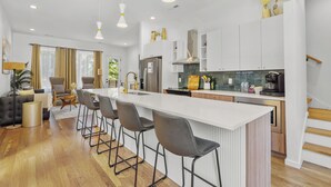 A modern kitchen with a central island, bar stools, and a dining area with a sofa and chairs. - Luxury Modern, Down Town Retreat, Pet Friendly (Chattanooga)