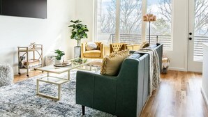 A living room with a green sofa, a coffee table, and a large window with a view of trees. - Luxury Modern, Down Town Retreat, Pet Friendly (Chattanooga)