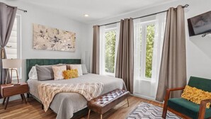 A bedroom with a bed, a bench, a chair, a lamp, and a painting on the wall. - Luxury Modern, Down Town Retreat, Pet Friendly (Chattanooga)