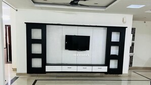 A spacious living room with a large TV mounted on a white cabinet, recessed lighting, and a tiled floor. - The Excellency Apartments (Hyderabad)
