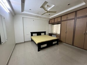 Een slaapkamer met een bed, kledingkast, plafondventilator en een raam met gordijnen.