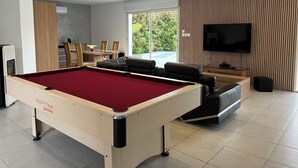 Ein modernes Wohnzimmer mit Billardtisch, einer Couch, einem Fernseher und einem Essbereich mit Stühlen und Tisch.