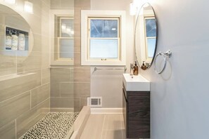 Un baño moderno con ducha, tocador, ventana y espejo.