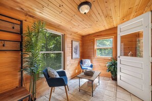 L’intérieur chaleureux d’un chalet avec des murs en bois, une chaise bleue, une petite table et une grande fenêtre donnant sur la forêt.