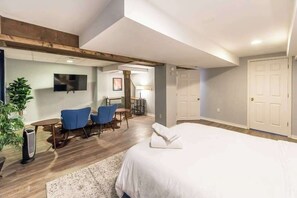 A hotel room with a large bed, a desk with chairs, a TV, and a plant.