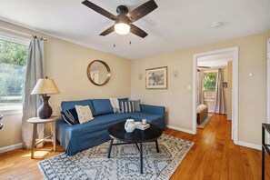 A living room with a blue sofa, a round mirror, a ceiling fan, and a coffee table. - Large 4BR Home, Walk to Downtown A2 (Ann Arbor)