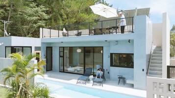 Ein modernes, zweistöckiges Haus mit Balkon, Schwimmbad und Terrassenbereich.
